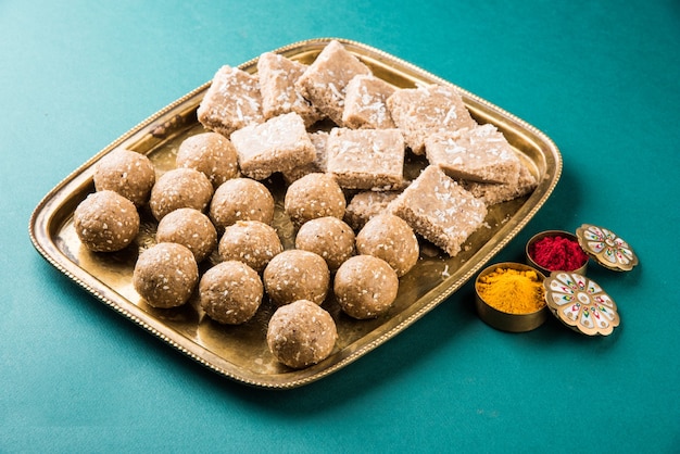 Photo sesame or ril gul or tilgul laddu with haldi kumkum with flowers for makar sankranti festival, selective focus