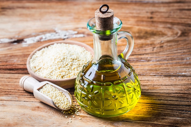 Sesame seeds and bottle with oil on a old wooden table?Sesame oil oil in a glass jug.