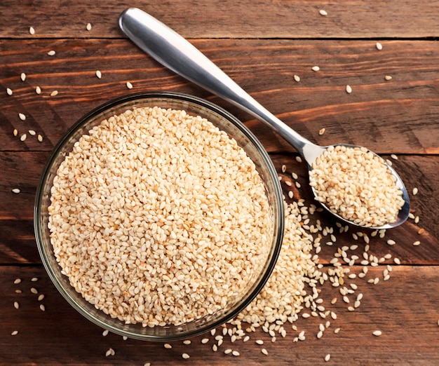 Sesame seeds in a plate and spoon close-up on a wooden background. Top view
