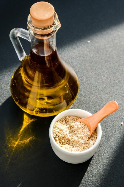 Sesame with oil in glass bottle. Healthy food concept. Vegan keto diet. Sesame oil Minimalistic concept on dark background with deep shadows.