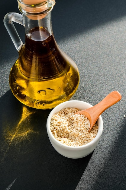 Sesame with oil in glass bottle. healthy food concept. vegan keto diet. sesame oil minimalistic concept on dark background with deep shadows