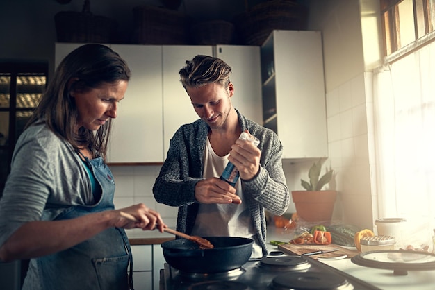 Sesoning to perfection Shot of a mother and her adult son cooking together in their kitchen at home