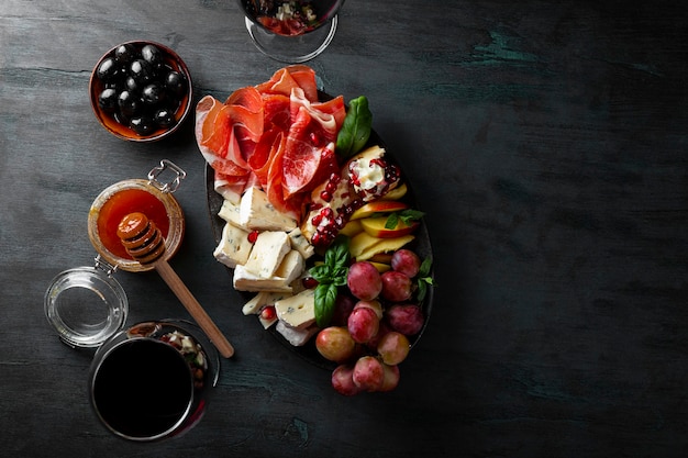 A set of appetizers for wine, jamon, pepperoni, cheese, grapes, peach and olives on a plate top view.