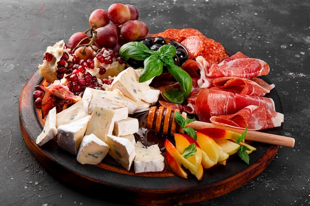 Foto una serie di antipasti per vino, prosciutto, peperoni, formaggio, uva, pesche e olive su una tavola di legno da vicino. snack board su sfondo grigio scuro. foto di alta qualità