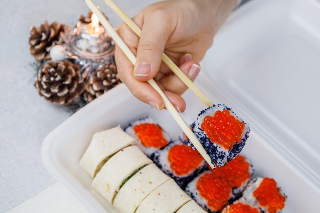 A set of Asian rolls in a plastic box at home in the kitchen in a festive style The girl is holding food with chopsticks Christmas concept Decorations for the New Year