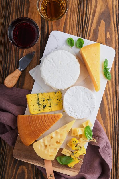 Set or assortment cheeses Maasdam smoked cheese camembert blue cheese parmesan brie cheese with basil and pepper on on white marble board brown wooden old background Top view Free copy space