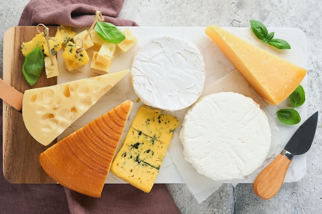 Set or assortment cheeses Maasdam smoked cheese camembert blue cheese parmesan brie cheese with basil and pepper on on white marble board white wooden old background Top view Free copy space