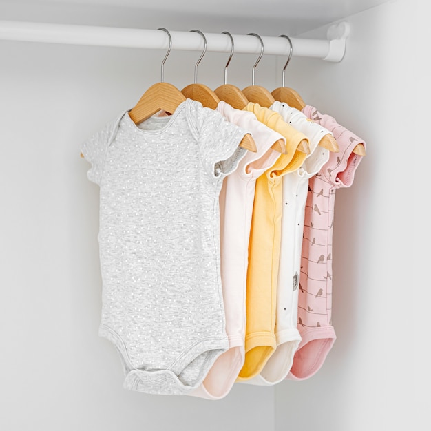 Set of baby bodysuits for a newborn girl and boy on hangers in white wardrobe. Motherhood, cleaning home kids wardrobe. Minimal fashion concept.