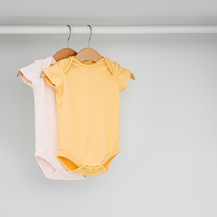 Photo set of baby bodysuits for a newborn girl and boy on hangers in white wardrobe. motherhood, cleaning home kids wardrobe. minimal fashion concept.