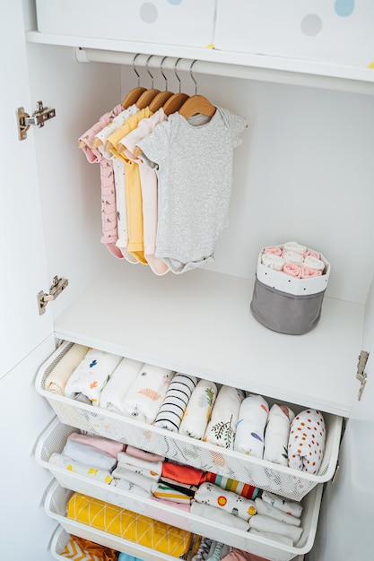 Set baby bodysuits voor een pasgeboren meisje en jongen op hangers in witte kledingkast. moederschap, kindergarderobe opruimen. minimaal modeconcept.