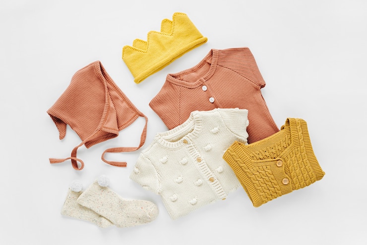 Photo set of  baby rompers, hat,  socks and  knitted jumper on white bed. gender neutral baby clothes and accessories. flat lay, top view