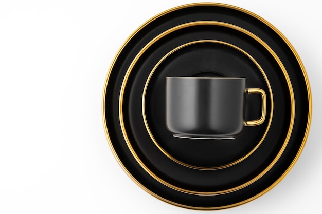 A set of black and golden ceramic plates and cup on a white background Top view