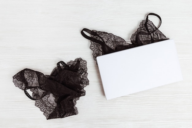 Set of black lingerie in white box. Mock up. Fashionable female underwear on wooden background.