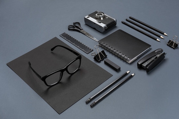 Foto un set di accessori per ufficio neri, occhiali e vecchia macchina fotografica su sfondo grigio. disposizione piatta. natura morta. modello