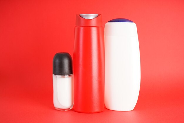 Photo set of bottles of shampoo and deodorant on red background.