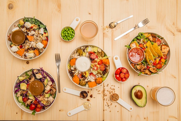 Set of bowls of healthy fresh and summer salads with fruits Mexican avocados split cherry tomatoes soy beans and lettuce with sauces on a pine wood counter