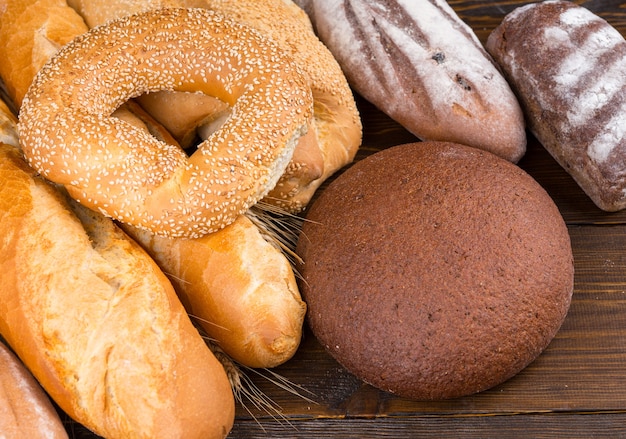 Set of breads with examples of sesame seed bagels, baguettes, rolls and artisan loaves on dark wood table