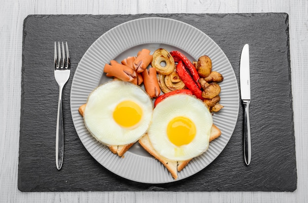 Set for breakfast fried eggs, grilled vegetables, sausages. Bread on a wooden table.