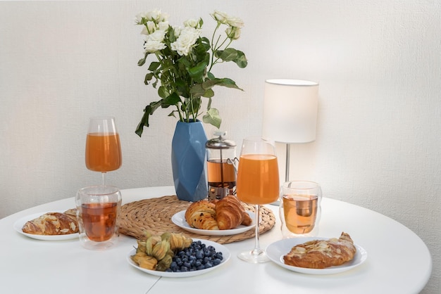 A set breakfast table with a bouquet of flowers a lamp cups of tea glasses of juice and croissant