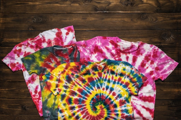 Photo a set of bright tie dye t-shirts on a wooden background. flat lay.