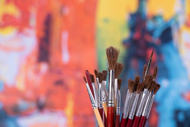 Photo set of brushes in a jar in front of an abstract paint