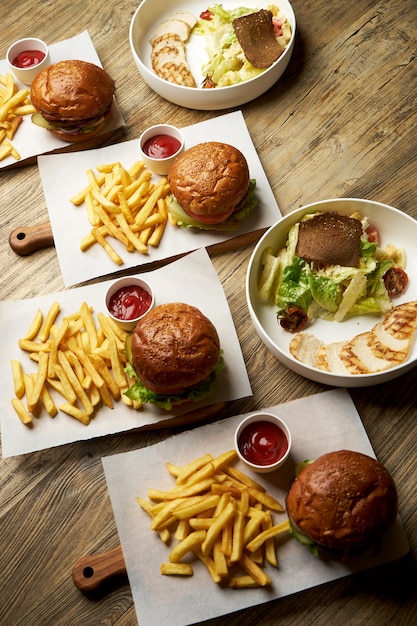 Set of burgers with french fries and ketchup sauce. Big hamburgers and french fries on wooden table background. Fast food set background. Restaurant burger menu