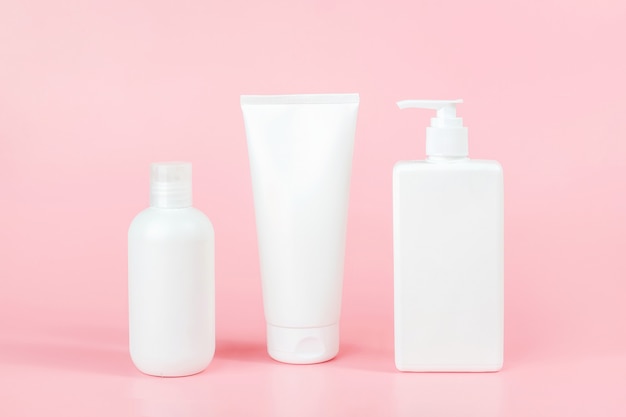 Photo set of care cosmetic for skin, body or hair. three white blank cosmetics bottles on pink