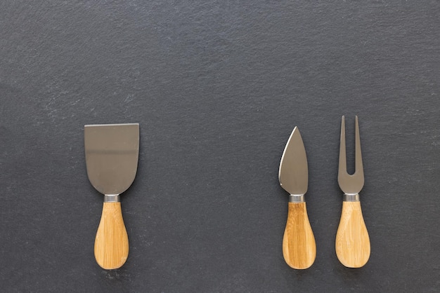 Set of cheese knives with wooden handles Fork and spatula on black background