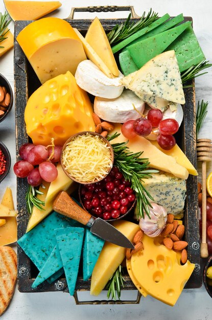 Set of cheeses with snacks in a wooden box on a white wooden\
background free copy space