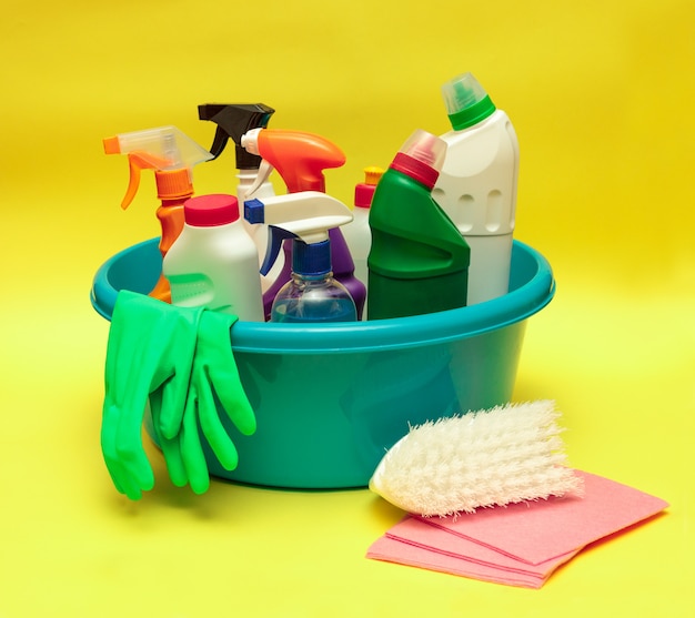 Set of cleaning products and detergents in a blue basin on a yellow background