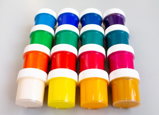 A set of closed jars with gouache of different colors are laid out in rows on a gray background hobby - drawing