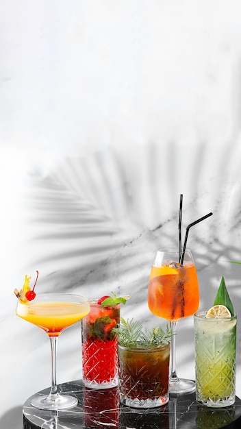 Impostare cocktail sul tavolo di marmo e banner di sfondo chiaro. cinque tipi di cocktail estivi colorati in bicchieri e ombra di ramo tropicale sullo sfondo. mojito, aperol spritz, margarita