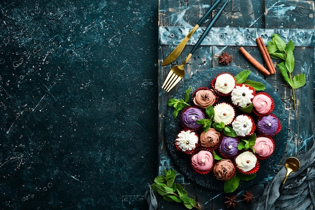 Set of colored cream muffins on a black plate with mint Top view Rustic style