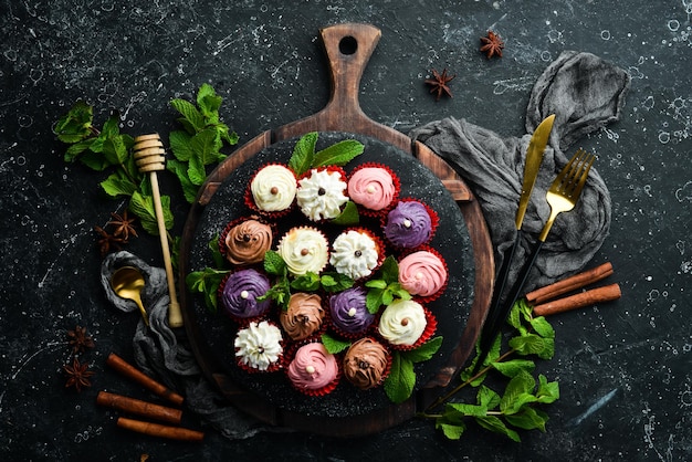 Set of colored cream muffins on a black plate with mint Top view Rustic style