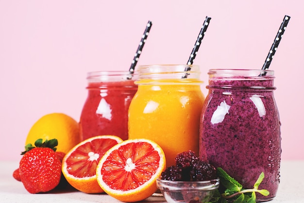 Set of colored fresh fruit smoothies on a light pink background.