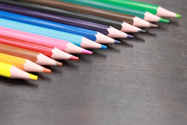 A set of colored pencils on a black wooden background. Sharpened bright pencils