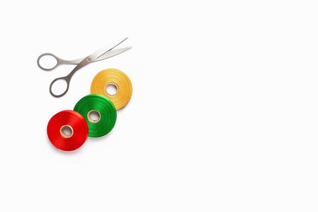 Photo set of colorful satin ribbon spools and scissors on white background top view copy space