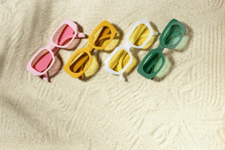 Set of colorful sunglasses on beach sand background at sunlight palm shadow Summer fashion eyeglasses with colored glass Summer vacation summer rest concept Minimal style flat lay above view