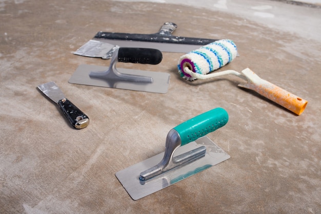 Photo set of construction tools, decorative plaster knives, paint roller, construction mockup on concrete floor