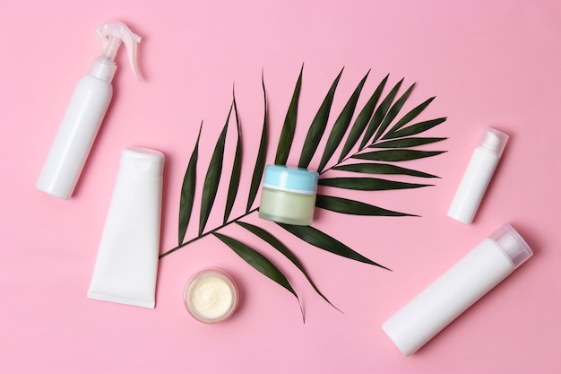 Set of cosmetic jars of white color and palm branches on a colored background top view close up. High quality photo