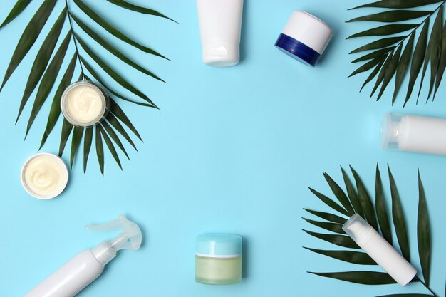 Set di vasetti cosmetici di colore bianco e rami di palma su uno sfondo colorato