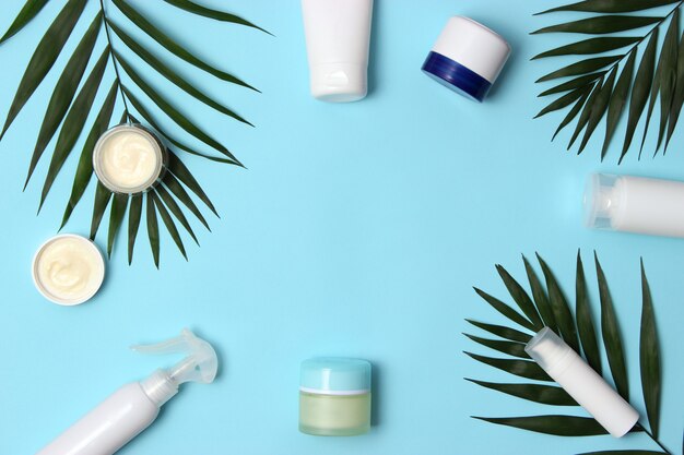 Set of cosmetic jars of white color and palm branches on a colored background