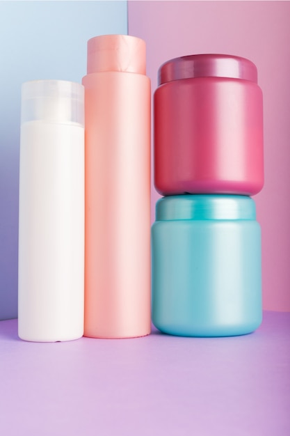 Set of cosmetic products on pink wall. Cosmetic package collection for shampoo, mask, conditioner, shower gel. Pink, white, blue plastic bottles, jar for packaging cosmetics