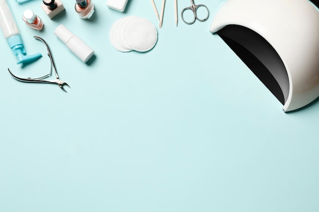 A set of cosmetic tools for manicure and pedicure on a blue background. Gel polishes, nail files and clippers, and the lamp top view  Place for text. Top view. Flat lay