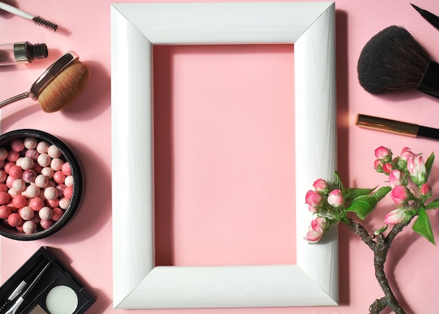 A set of decorative cosmetics on a pink wall with a white frame in the center. Top viev. Flat lay.