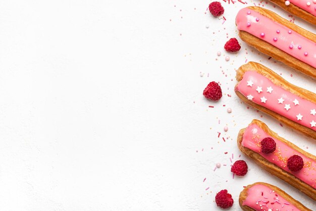 Set di deliziosi bignè con glassa di lampone rosa e granelli di zucchero su sfondo bianco.