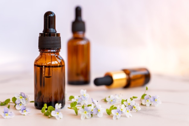 Set of different bottles with beauty serum, hyaluronic acid and vitamins on light surface with wild flowers