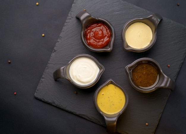 Photo set of different bowls of various dip sauces on dark background top view
