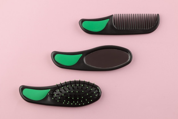 A set of different hair brushes and a mirror in one style on a bright pink background. view from above