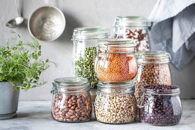 Set of different legumes in glass jars on, concrete white table. a source of protein for vegetarians. the concept of healthy eating and food storage.